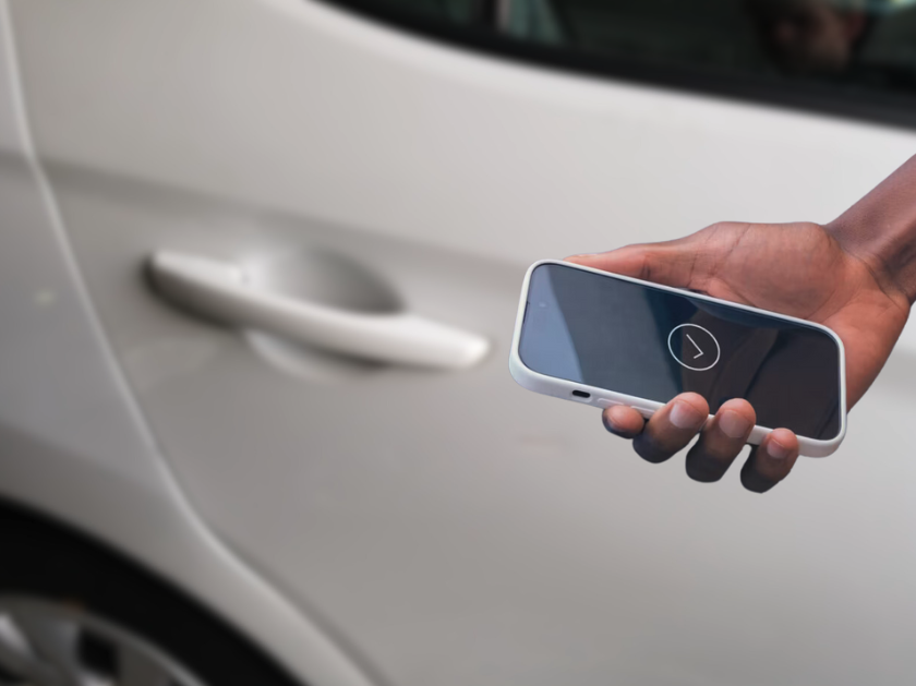 Person holding a smartphone with Hyundai Digital Key app near the door handle of a white Hyundai vehicle